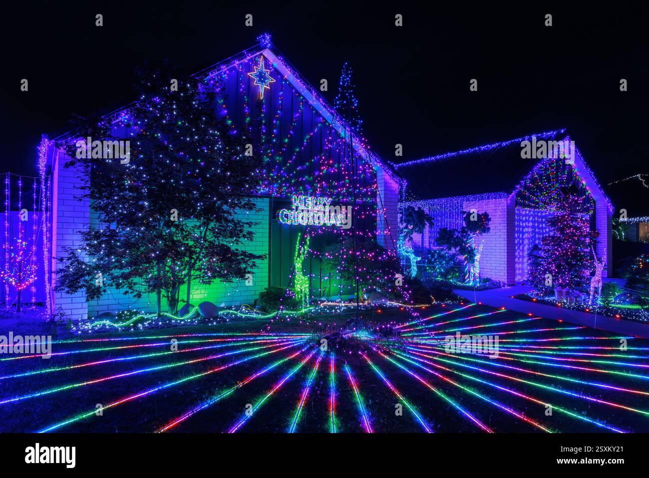 Una casa suburbana di notte coperta di luci natalizie, che corre anche attraverso il prato e il giardino Foto Stock