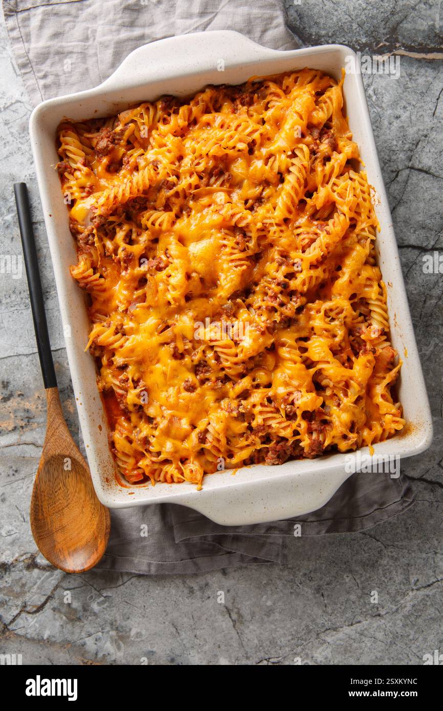 La casseruola Sloppy Joe è piena di carne macinata succosa e pasta soffocata in un primo piano di salsa al formaggio nel piatto da forno sul tavolo. Vista dall'alto verticale Foto Stock