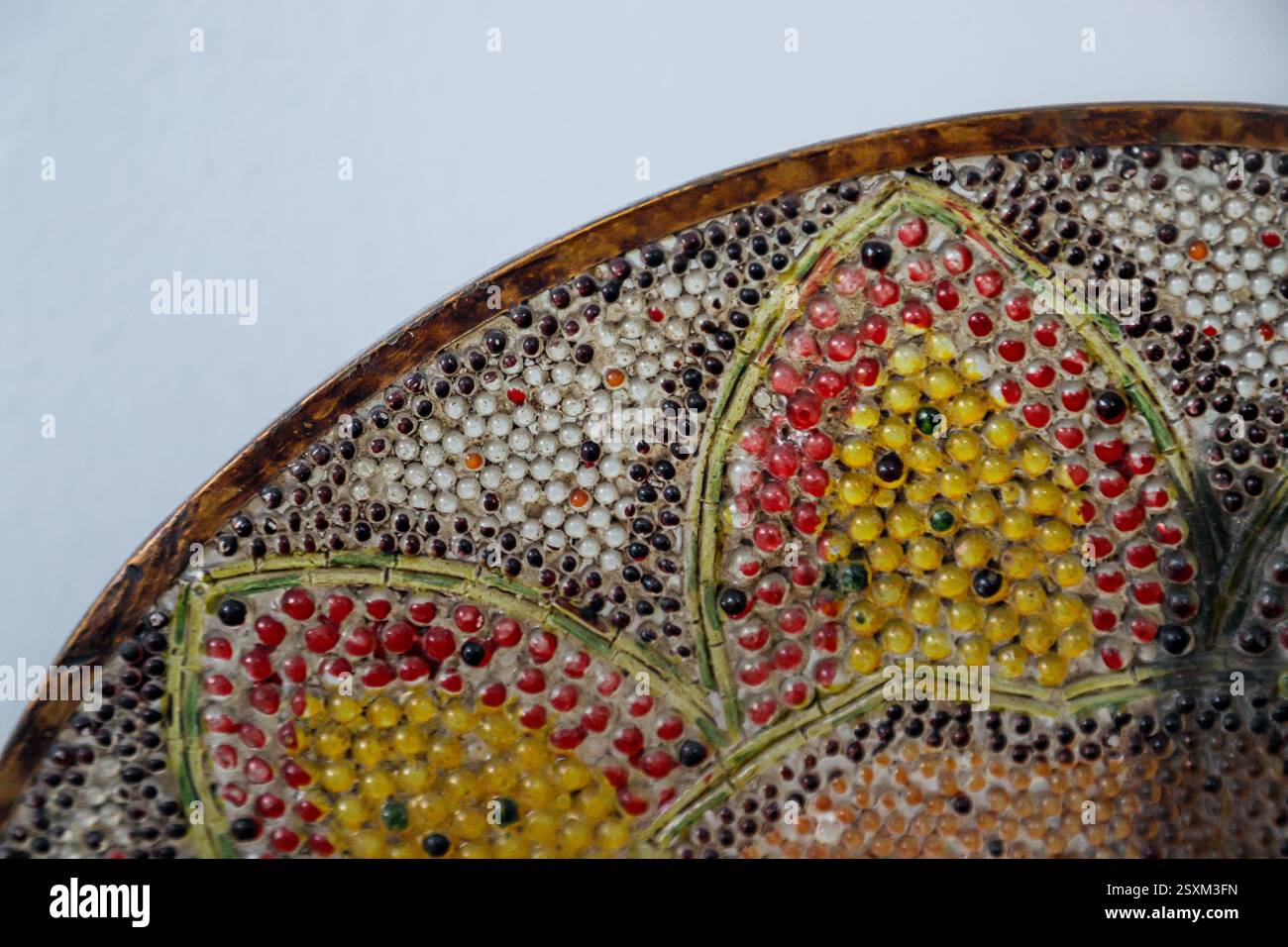 Questa ciotola decorativa presenta vivaci motivi floreali creati con perline colorate, mettendo in risalto l'abilità artigianale e il design artistico. Foto Stock