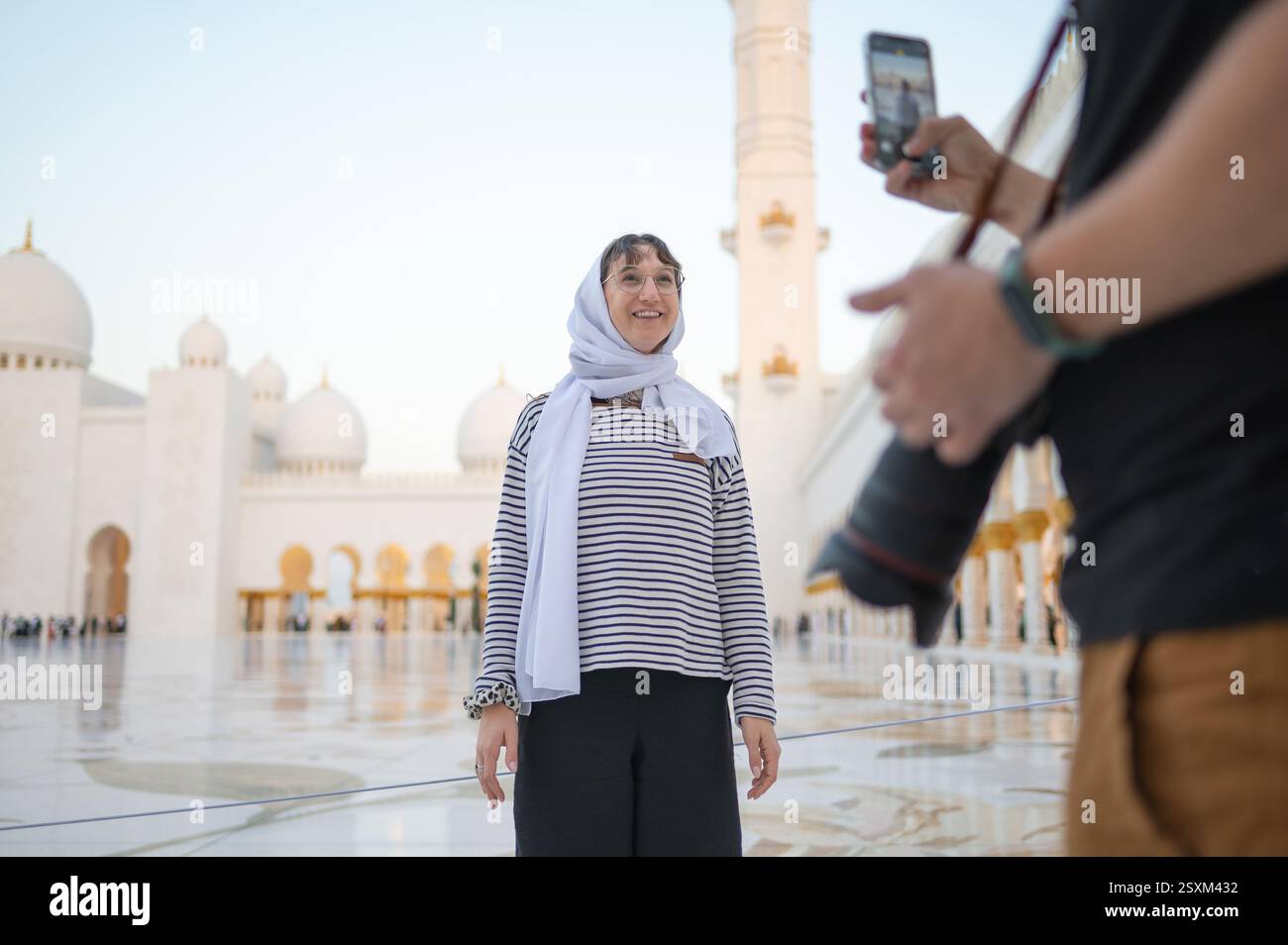 Un fotografo maschile scatta una foto di una donna con un foulard usando il suo telefono alla grande Moschea dello sceicco Zayed. Amici che visitano Abu Dhabi e creano Foto Stock