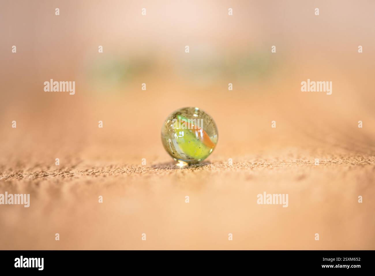 Un singolo marmo di vetro su una superficie di legno, caratterizzato da intricati motivi a turbolenza e luce riflessa, nostalgica e giocosa Foto Stock