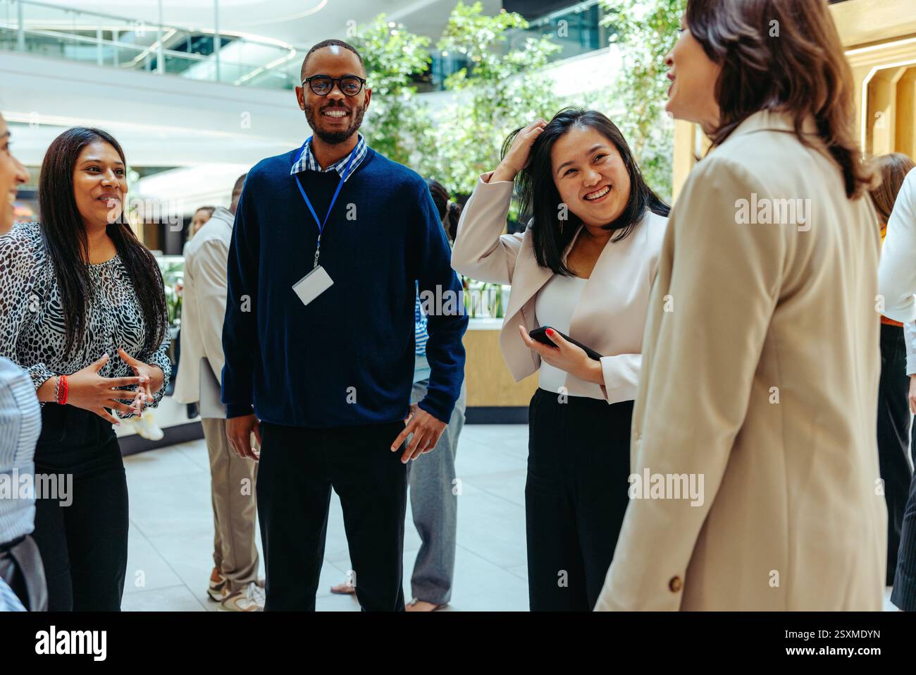 Un gruppo diversificato di professionisti si impegna in una riunione informale all'interno di un moderno cortile di uffici. L'ambiente è luminoso e aperto, favorendo la collaborazione Foto Stock
