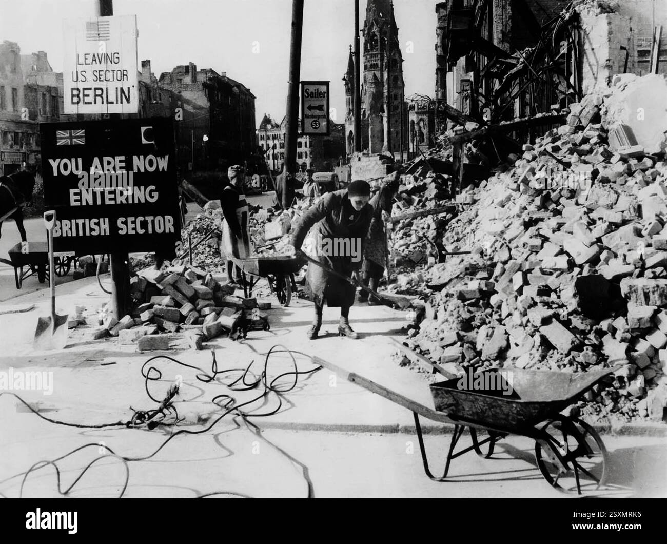 Donne tedesche che ripuliscono i detriti sulla Tauentzienstrasse di Berlino, con le rovine della Chiesa del Kaiser Guglielmo sullo sfondo. L'assenza di uomini abili alla fine della guerra nel 1945 ha fatto sì che la responsabilità di ripulire il relitto ricadesse principalmente sulle donne civili, chiamate "Truemmerfrauen", o "signore delle macerie". I cartelli a sinistra segnano il confine tra il settore occupato dai britannici e il settore statunitense della città. Foto Stock
