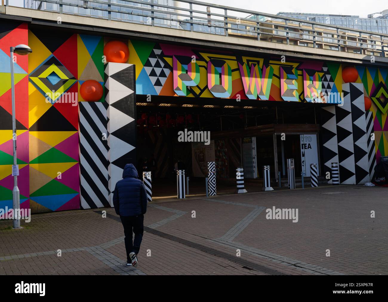 Uomo con cappuccio in piedi fino a un tunnel che porta alla centrale elettrica di Battersea, Londra, con il segnale DI ALIMENTAZIONE sopra. Foto Stock