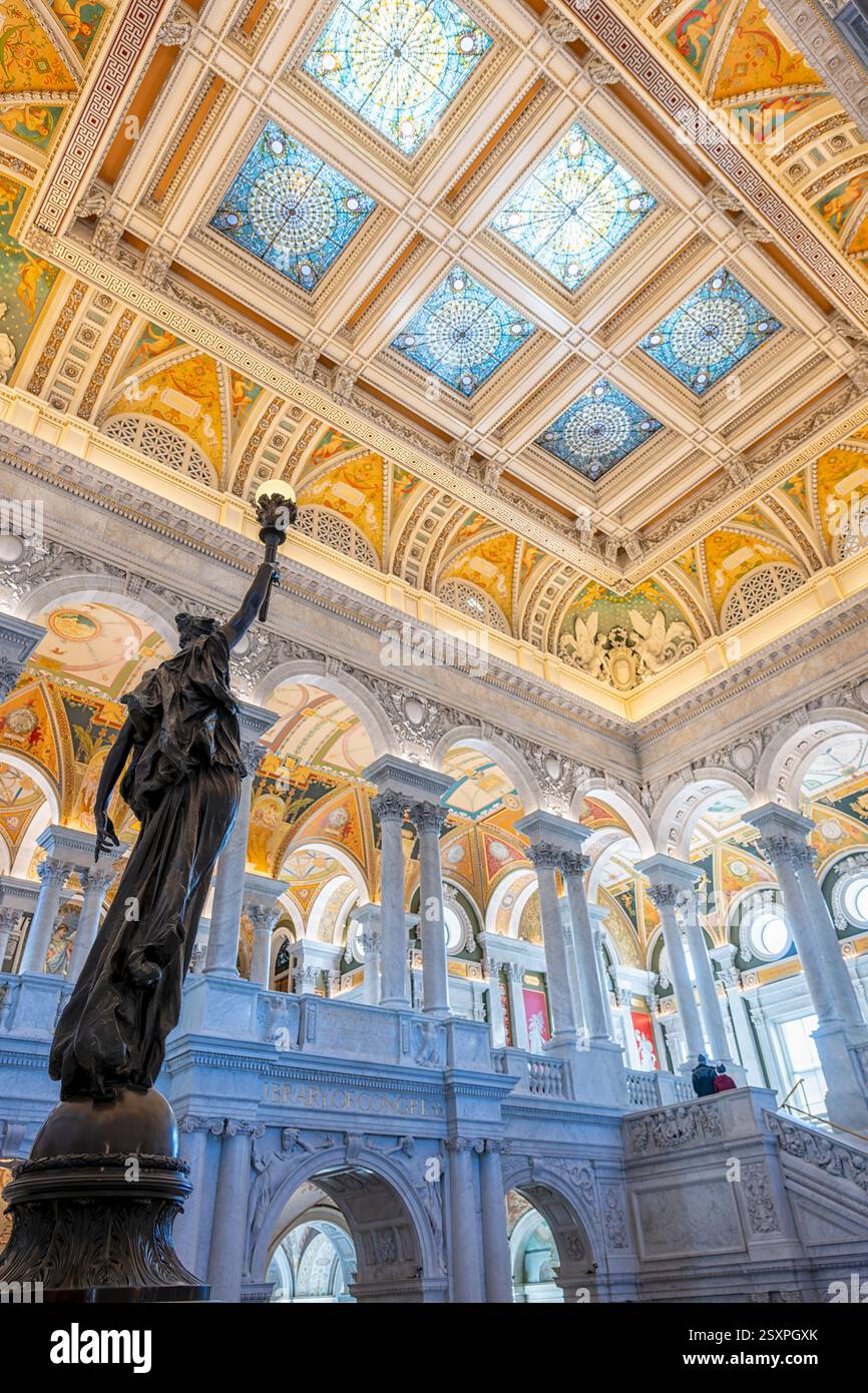 WASHINGTON DC - Una statua di bronzo di una figura femminile che tiene in alto una torcia elettrica si trova su un palo di newel nella sala principale della Biblioteca del Congresso Thomas Jefferson Building. Completata nel 1897, la figura femminile decorativa in bronzo simboleggia l'innovazione tecnologica americana nell'elettricità. La statua fa parte della decorazione ornata della grande scalinata in marmo nella sala grande e celebra i contributi americani alla scienza, in particolare la scoperta dell'elettricità di Benjamin Franklin, che ha permesso innovazioni come l'illuminazione elettrica prominente in tutto l'edificio. Foto Stock