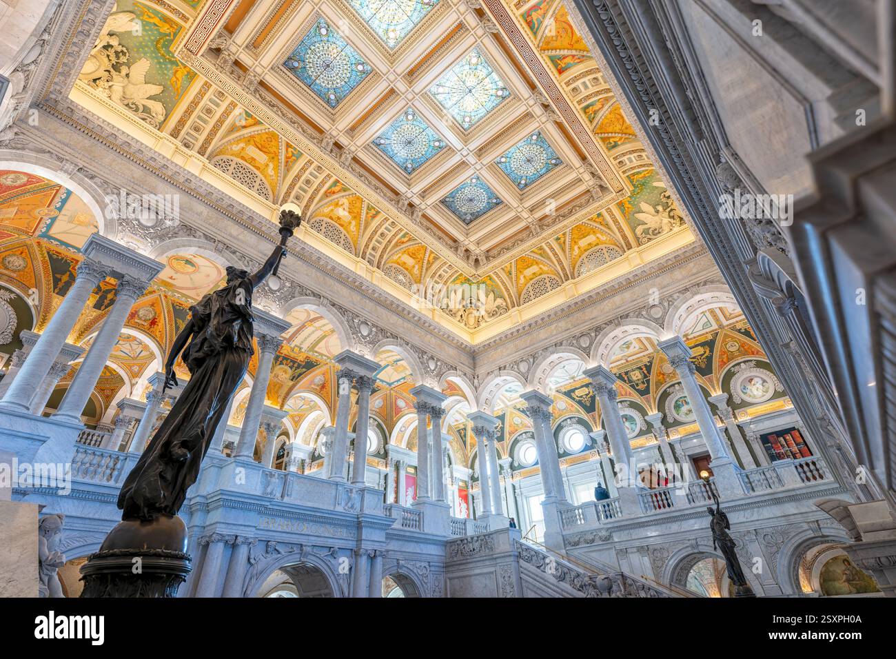 WASHINGTON DC - Una statua di bronzo di una figura femminile che tiene in alto una torcia elettrica si trova su un palo di newel nella sala principale della Biblioteca del Congresso Thomas Jefferson Building. Completata nel 1897, la figura femminile decorativa in bronzo simboleggia l'innovazione tecnologica americana nell'elettricità. La statua fa parte della decorazione ornata della grande scalinata in marmo nella sala grande e celebra i contributi americani alla scienza, in particolare la scoperta dell'elettricità di Benjamin Franklin, che ha permesso innovazioni come l'illuminazione elettrica prominente in tutto l'edificio. Foto Stock
