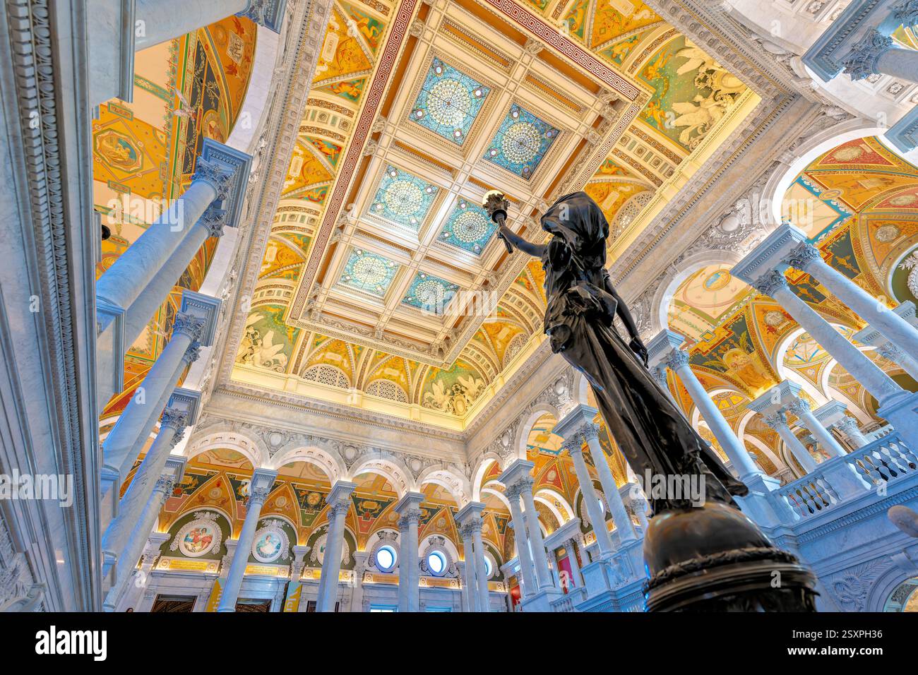 WASHINGTON DC - Una statua di bronzo di una figura femminile che tiene in alto una torcia elettrica si trova su un palo di newel nella sala principale della Biblioteca del Congresso Thomas Jefferson Building. Completata nel 1897, la figura femminile decorativa in bronzo simboleggia l'innovazione tecnologica americana nell'elettricità. La statua fa parte della decorazione ornata della grande scalinata in marmo nella sala grande e celebra i contributi americani alla scienza, in particolare la scoperta dell'elettricità di Benjamin Franklin, che ha permesso innovazioni come l'illuminazione elettrica prominente in tutto l'edificio. Foto Stock