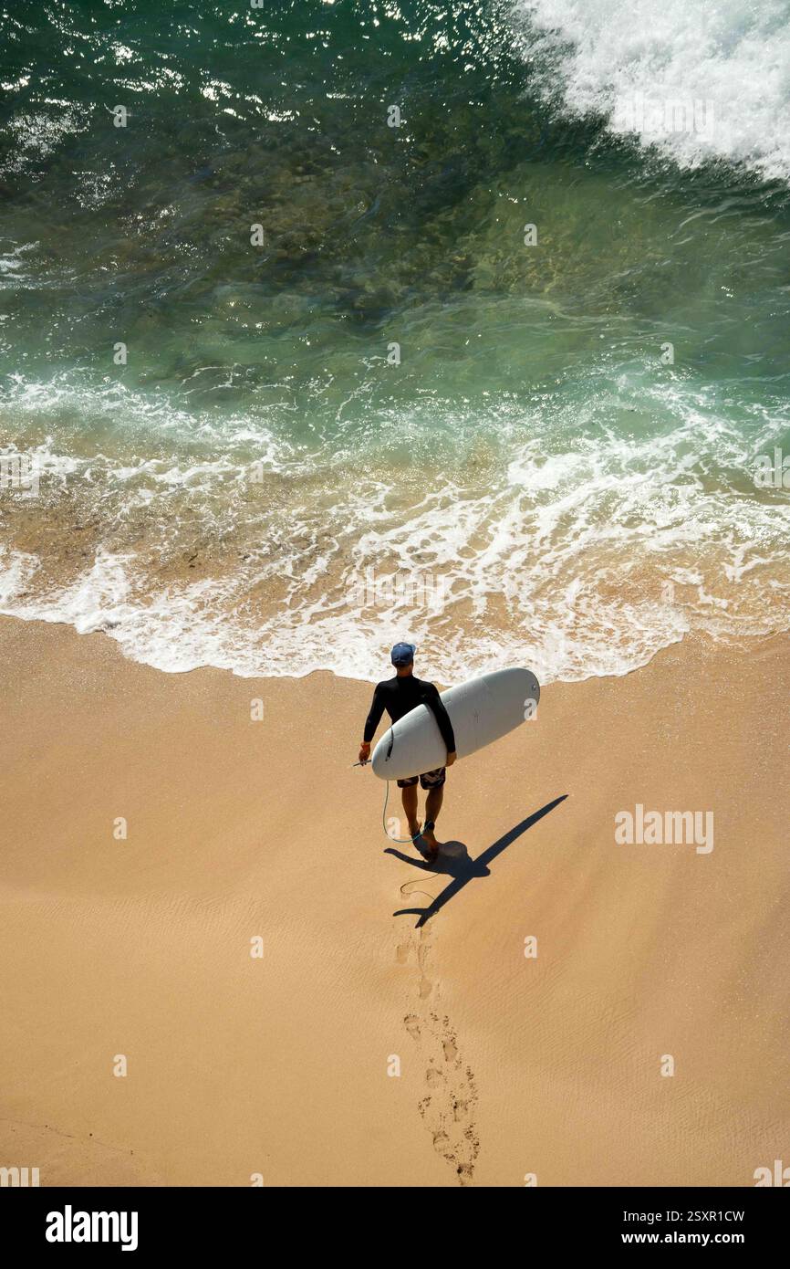 Bell'uomo sano che cammina sulla spiaggia tropicale Blue White Green Ocean Wave Breaking, entrare in acqua con tavola da surf bianca Foto Stock