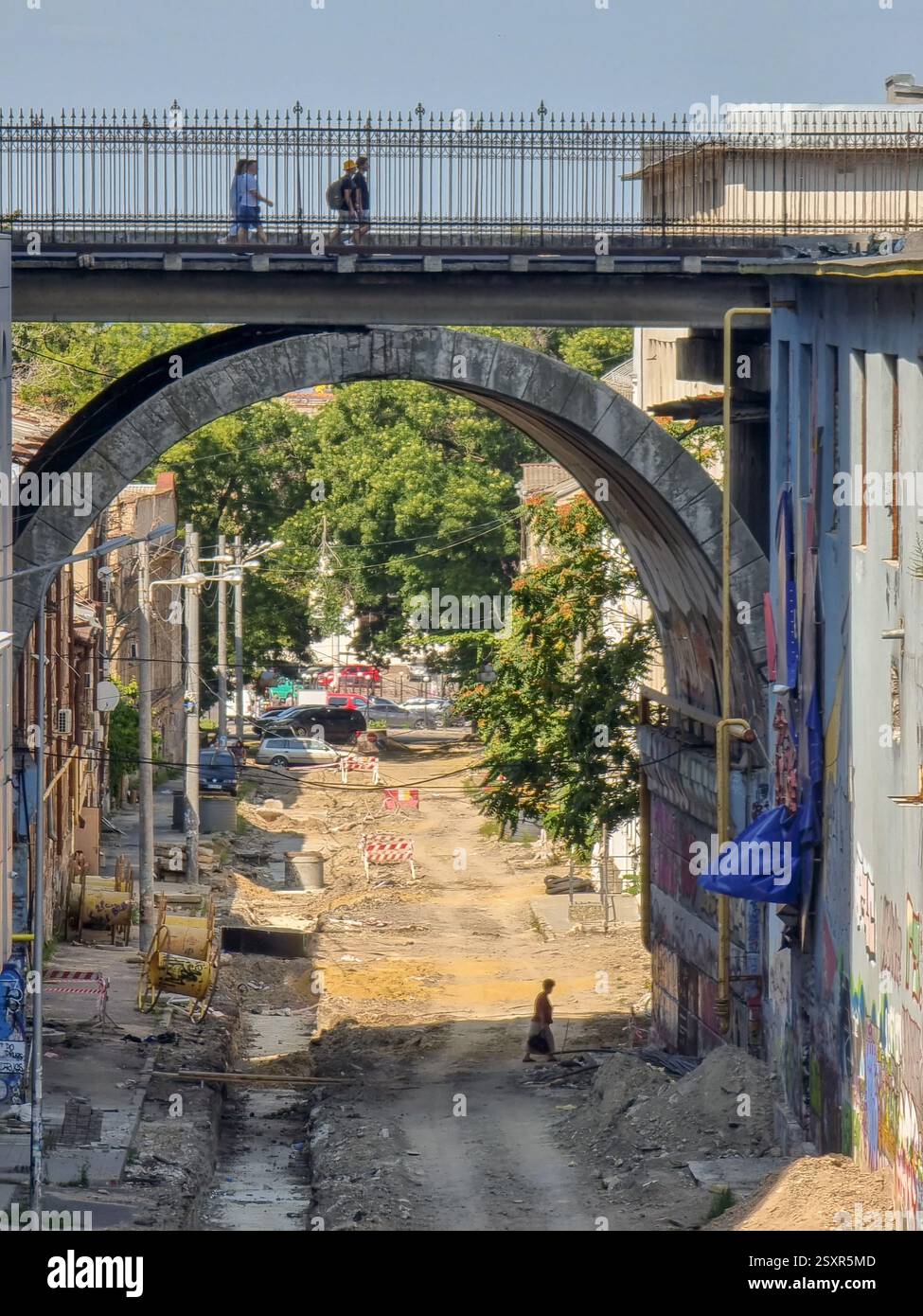 Persone che camminano su un ponte di pietra sopra una strada non asfaltata dove un'altra persona sta camminando; può essere un concetto per diversi livelli, due livelli, disuguaglianza - Immagine stock catturata con smartphone