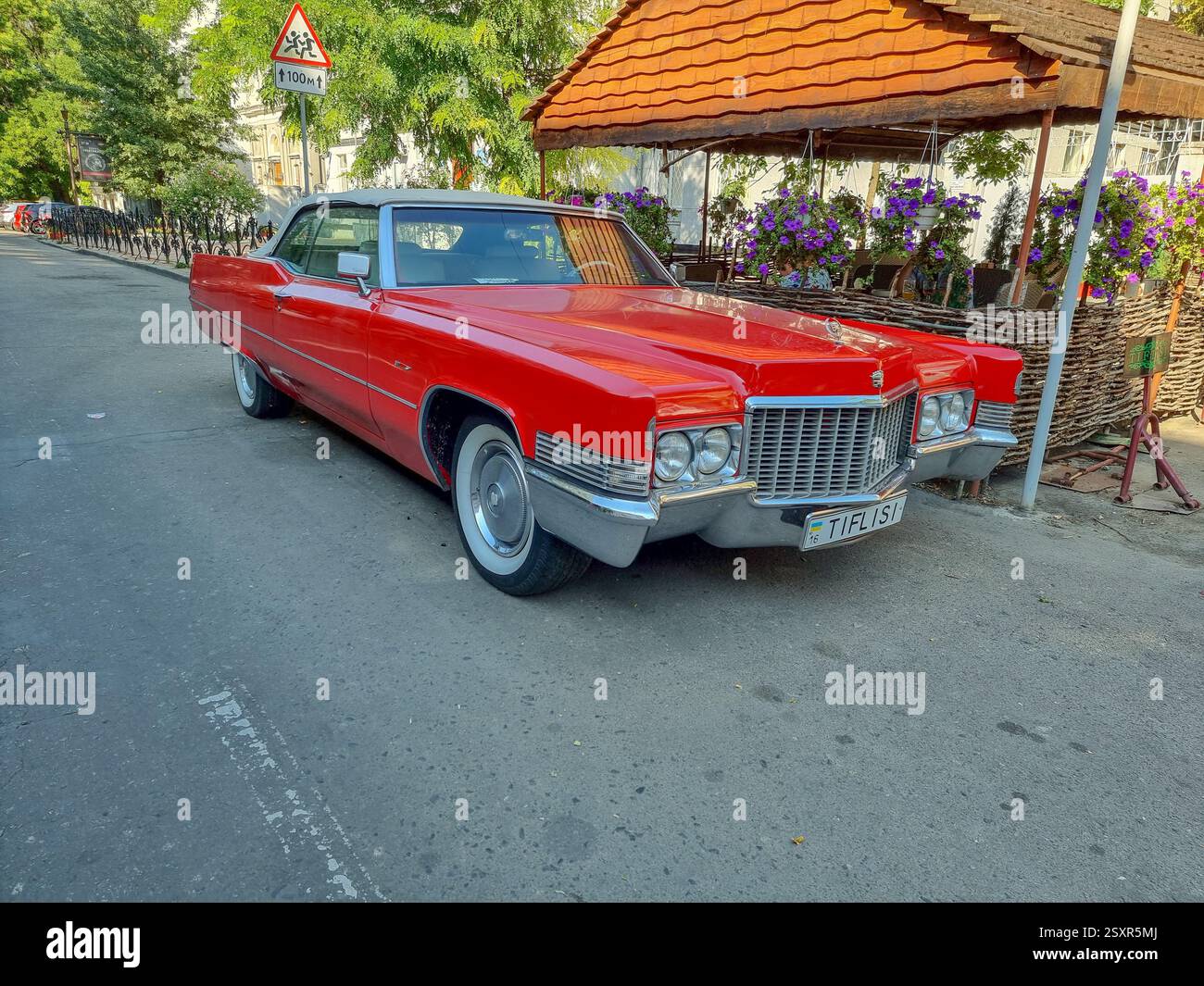Limousine americana rossa brillante: 1970 Cadillac DeVille cabriolet, davanti a destra; parcheggiata in una strada di fronte alla terrazza del ristorante a Odesa Foto Stock
