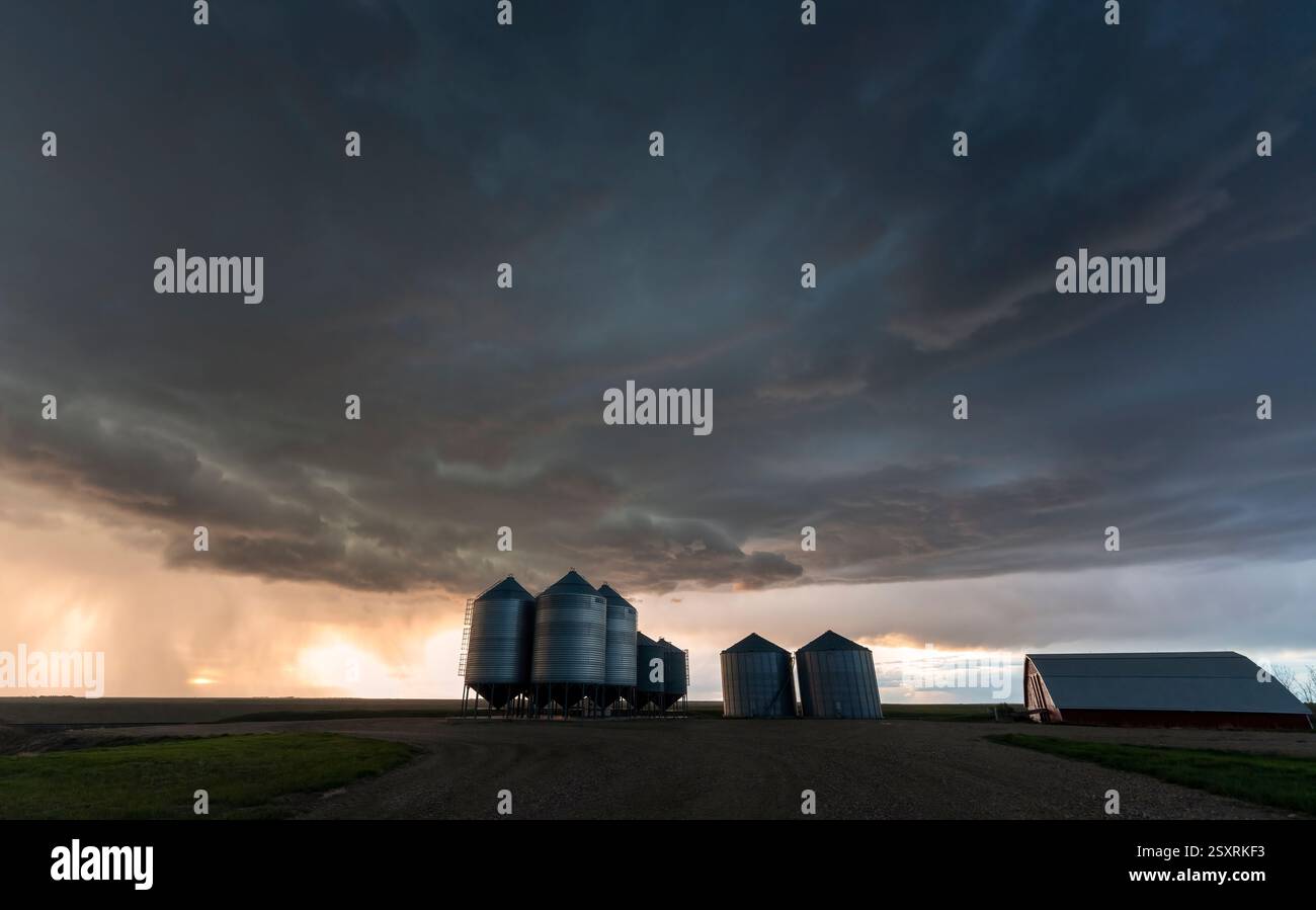 Nuvole di tempesta minacciose che si radunano sopra una fattoria al tramonto, creando una scena drammatica Foto Stock