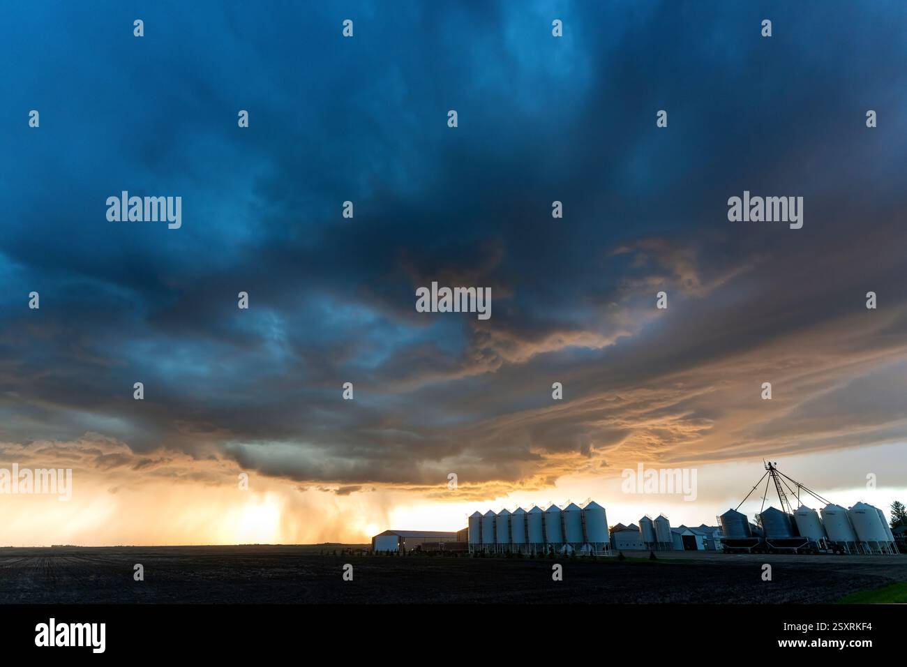 Spettacolari nuvole di tempesta che si radunano su una fattoria con silos di grano al tramonto, creando una scena potente e minacciosa Foto Stock