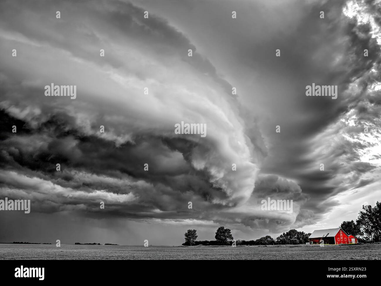 Il vivace fienile rosso è in netto contrasto con le spettacolari nuvole monocromatiche di supercell che si radunano sopra un campo Foto Stock