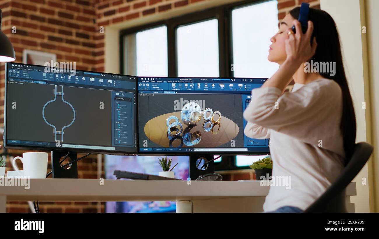 L'ingegnere professionista asiatico lavora sulla codifica di progetti industriali utilizzando strumenti software avanzati. Il soggiorno e l'ufficio sono dotati di due monitor e di apparecchiature tecniche per una produttività elevata. Telecamera B.. Foto Stock