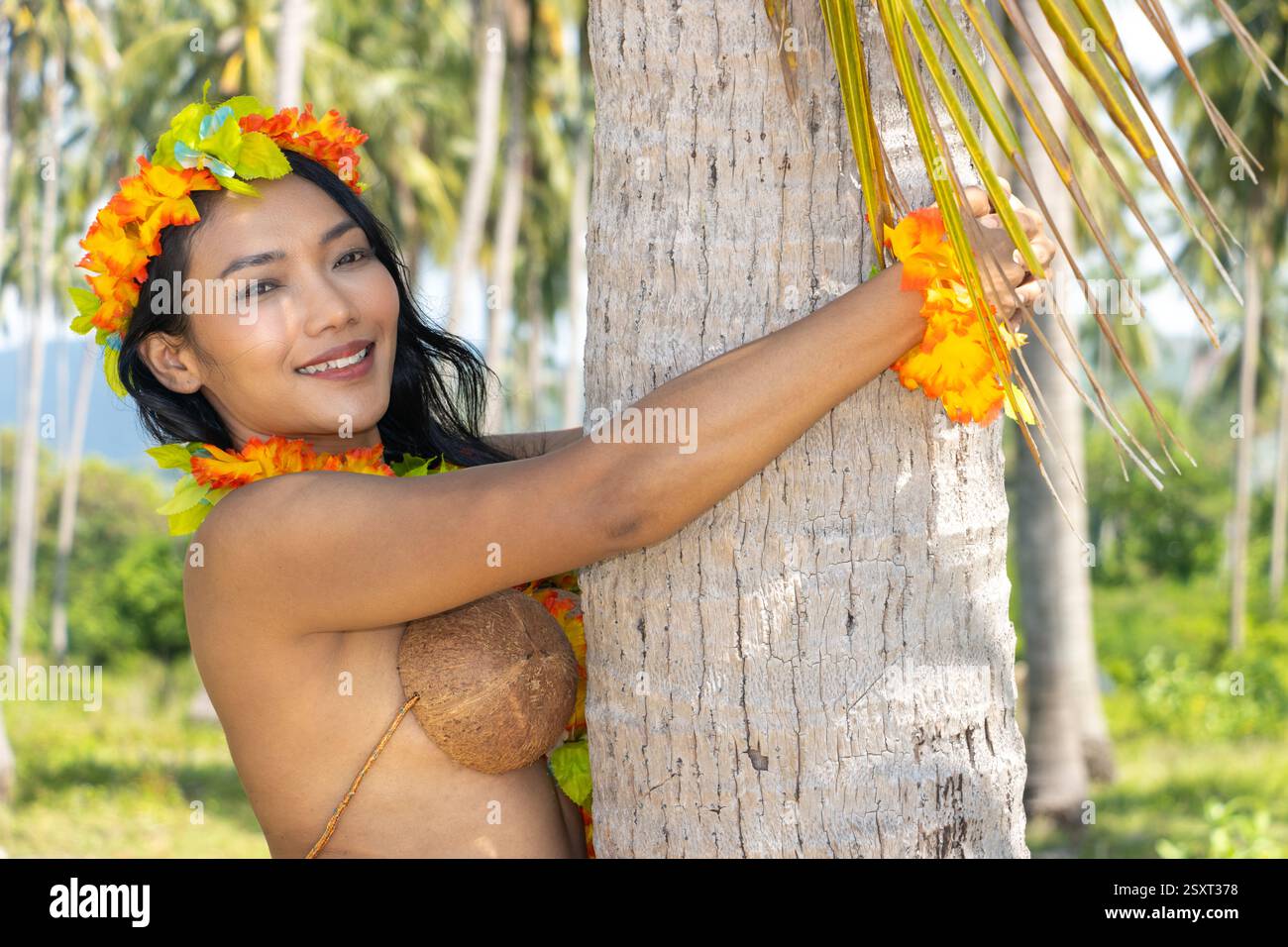 Hula ballerina delle Hawaii che abbraccia un albero di cocco Foto Stock