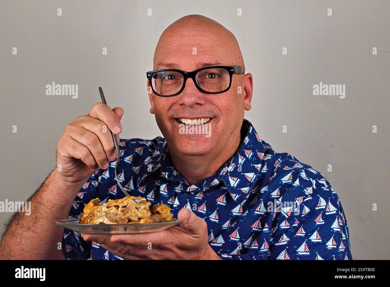 Un uomo isolato su uno sfondo bianco sorridente su un piatto di torta di mele. Foto Stock