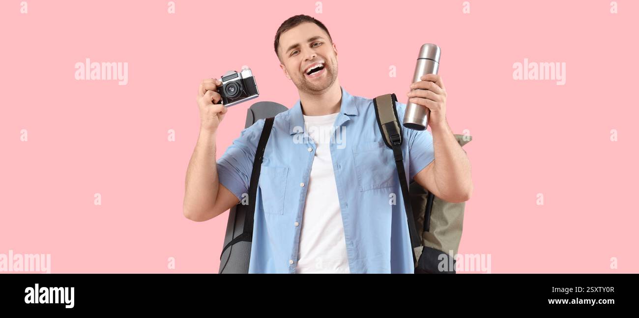 Turista maschile con zaino, thermos e fotocamera su sfondo rosa Foto Stock