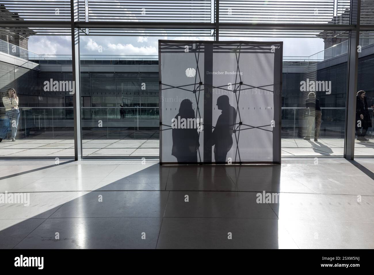 Bundestagsaufsteller auf der Fraktionsebene im Bundestag. Deutschland Berlin AM 25.02.2025: Ein grauer Aufsteller im Bundestag, der als Hintergrund für intervista Dient, Wird von der Sonne von hinten beleuchtet. Man sieht die silhouette des Gerüsts und zwei Menschen, die miteinander sprechen. *** Bundestag stand-up display a livello di gruppo parlamentare nel Bundestag Germania Berlino al 25 02 2025 Un stand-up grigio nel Bundestag, che funge da sfondo per interviste, è illuminato dal sole da dietro si può vedere la sagoma dell'impalcatura e due persone che parlano con Foto Stock