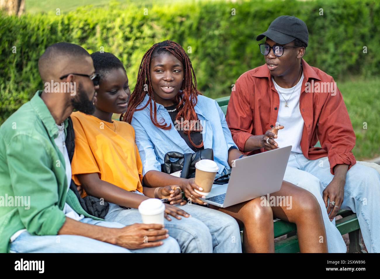 Gruppo di amici interrazziali che si godono un caffè nel parco con computer portatili, chiacchierano, si rilassano e si freelance Foto Stock