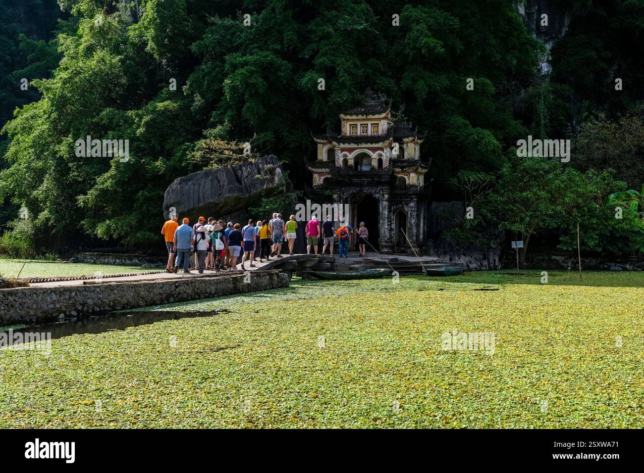 Un gruppo di turisti cammina fino all'ingresso del complesso del tempio di Bích Động, costruito nel 1428, vicino al villaggio di Tam Coc. Foto Stock