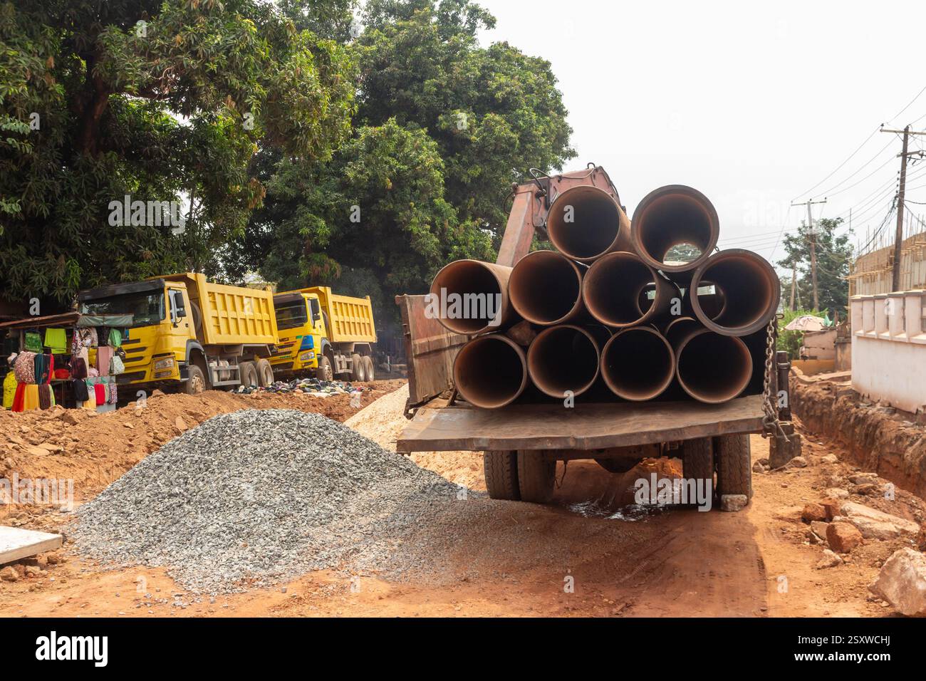 sito del progetto di sviluppo urbano con camion e pianale che trasportano tubi industriali, enugu, nigeria Foto Stock