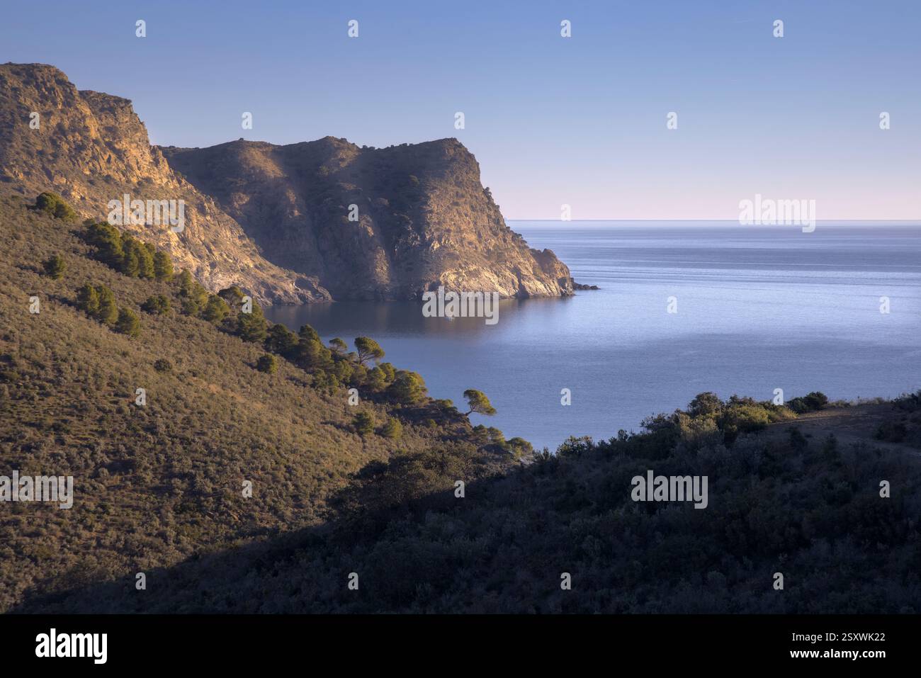 La luce dorata avvolge le aspre scogliere di Cap Norfeu, riflettendo tranquilli sulle calme acque della Costa Brava, in Catalogna Foto Stock