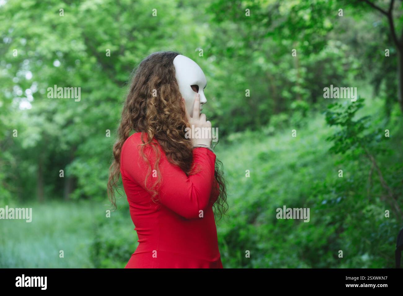 una donna misteriosa con maschera vaga nel mezzo di una foresta verde Foto Stock