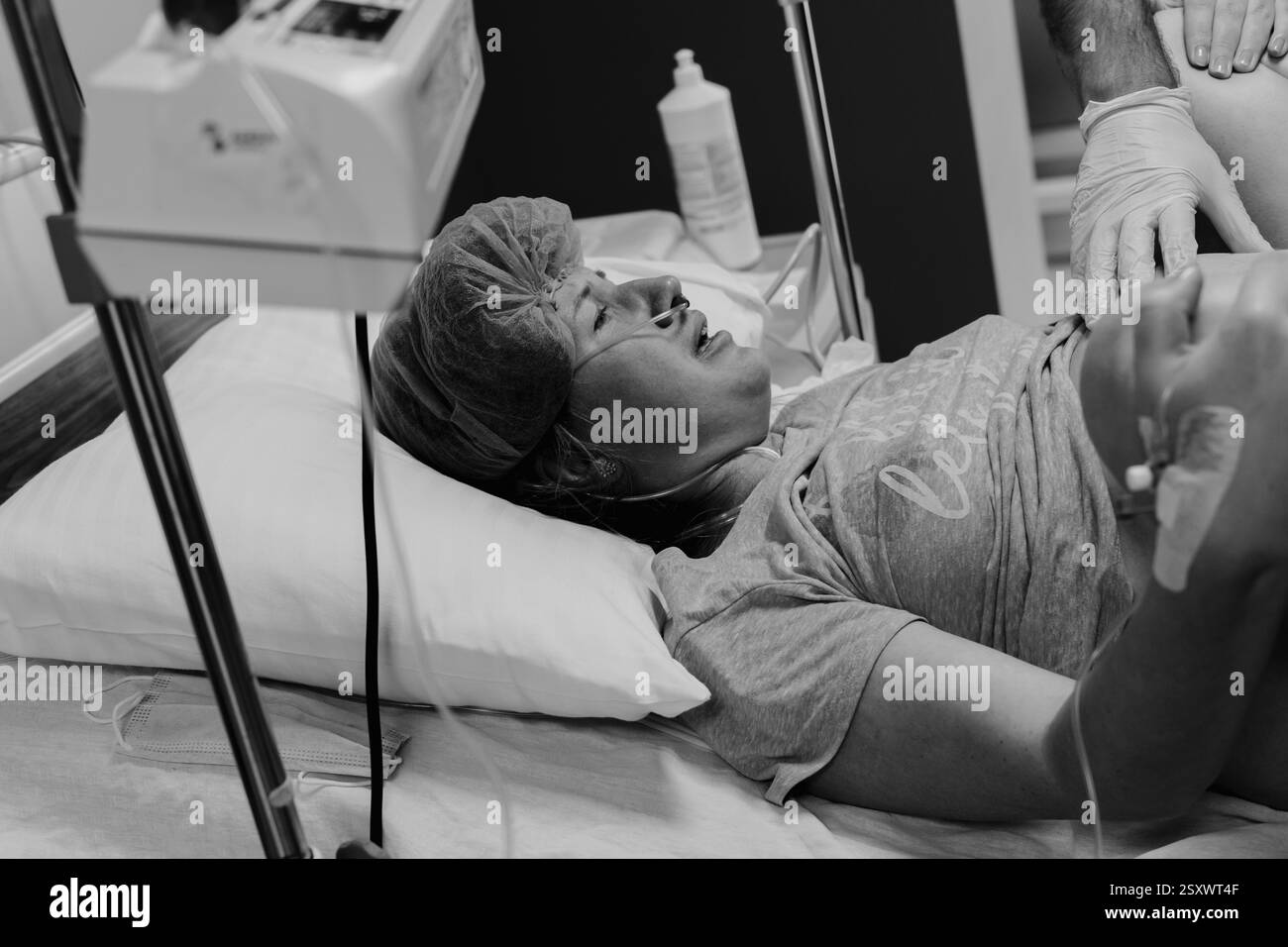 Un momento toccante di parto in un ospedale. I medici e il personale assistono la madre mentre il padre condivide la gioia dei primi momenti del neonato. Foto Stock