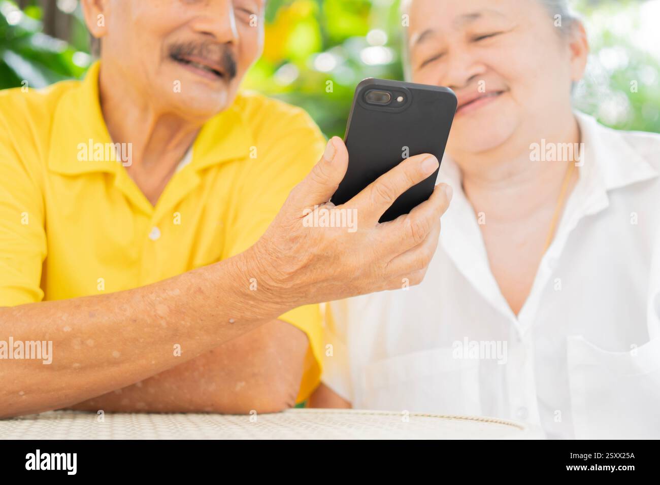 Una coppia attiva e sorridente seduto sulla sedia da giardino e guardando lo smartphone. Uso della tecnologia moderna da parte degli anziani. Foto Stock