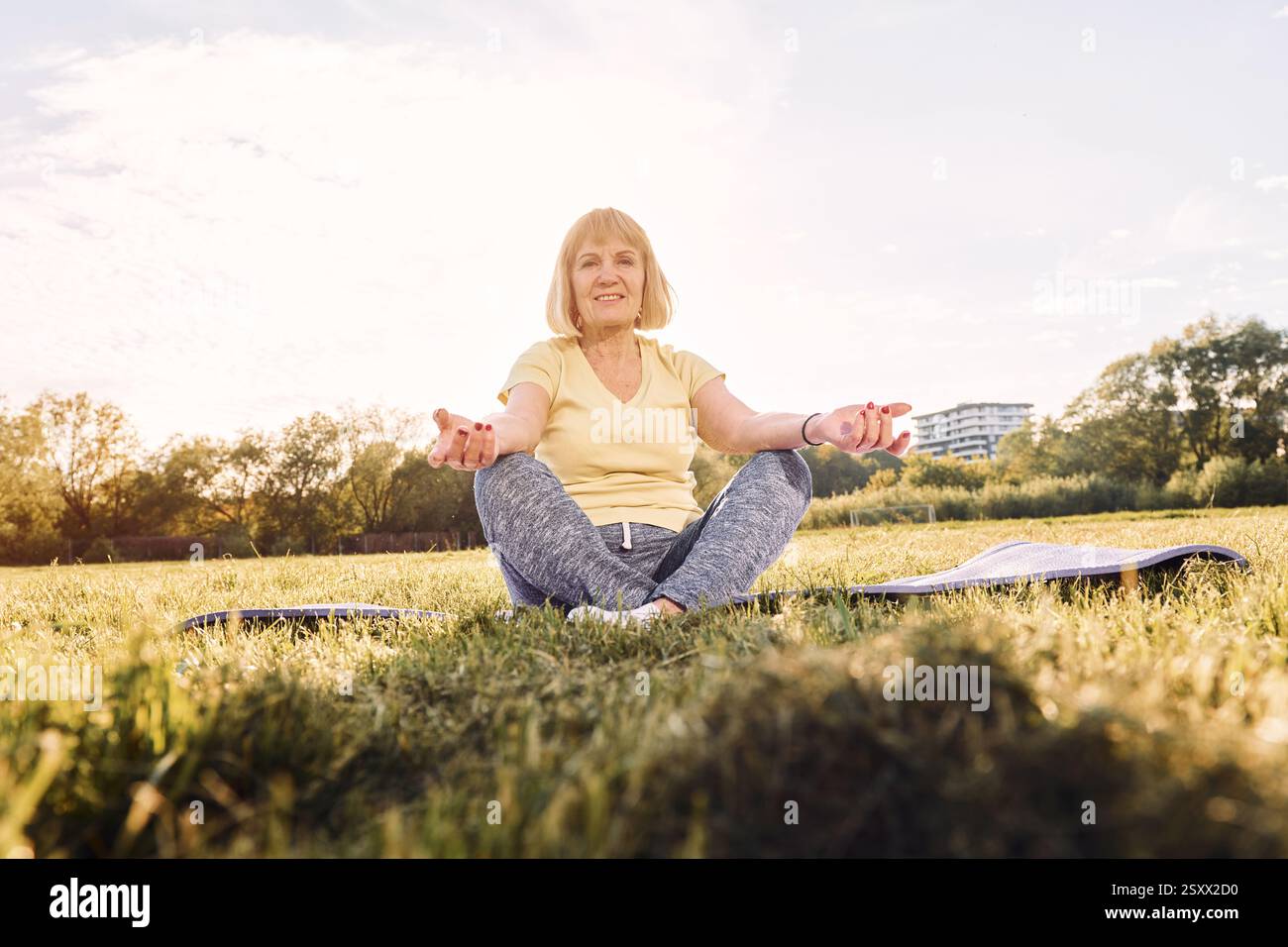 Fare esercizi di yoga. Donna anziana che trascorre un bel fine settimana all'aperto sul campo durante la giornata di sole. Foto Stock
