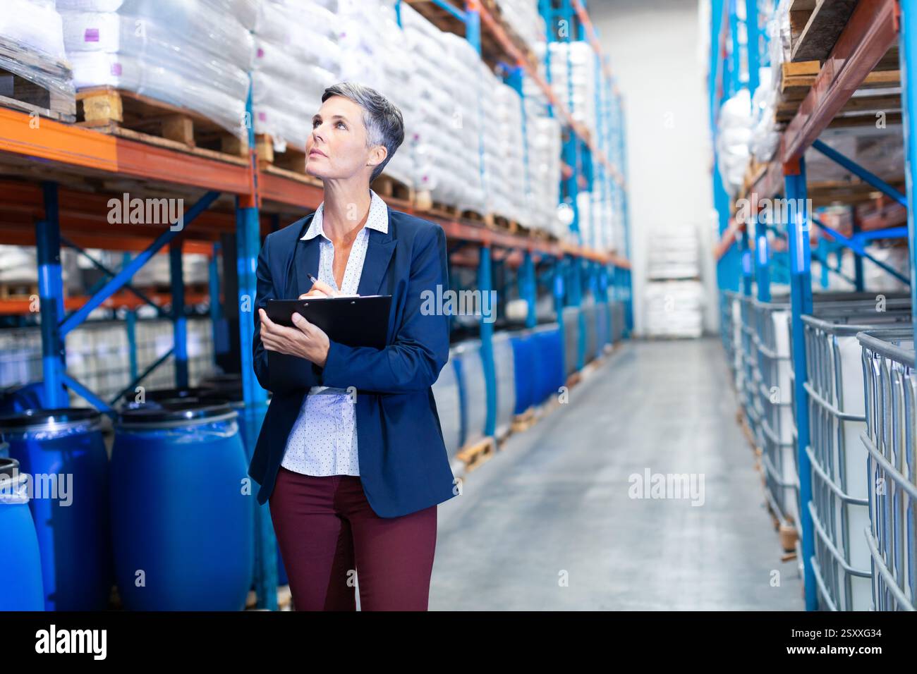 Donna professionista che ispeziona l'inventario con gli appunti in un'ampia corsia di magazzino Foto Stock