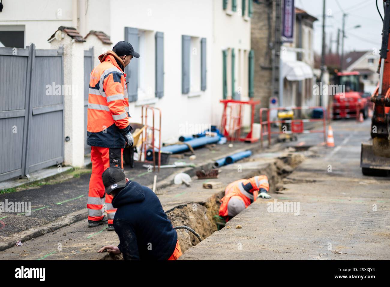 Lavoratori edili che riparano una strada urbana con attrezzature, barriere e macchinari di sicurezza. Infrastruttura e manutenzione. Foto Stock