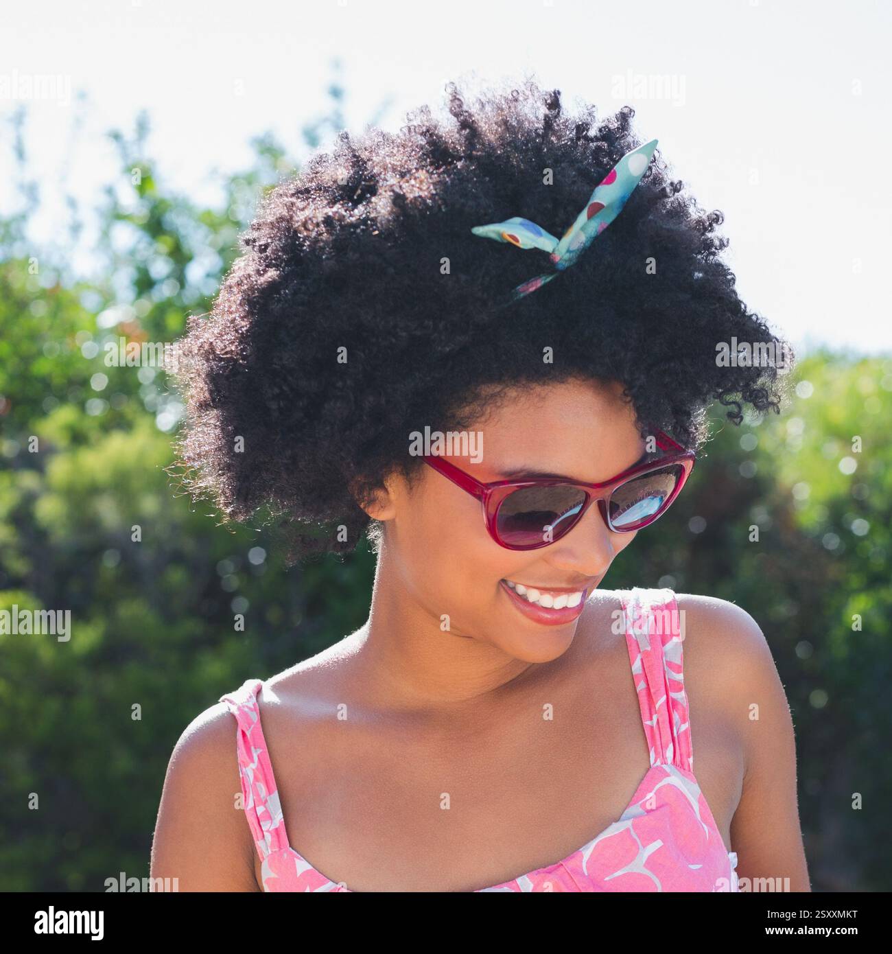 Donna sorridente che indossa gli occhiali da sole e si gode la giornata all'aperto con un abito estivo Foto Stock