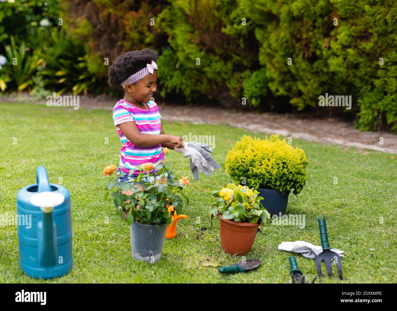 Giovane ragazza giardinaggio nel giardino, indossa guanti e sorride con le piante Foto Stock