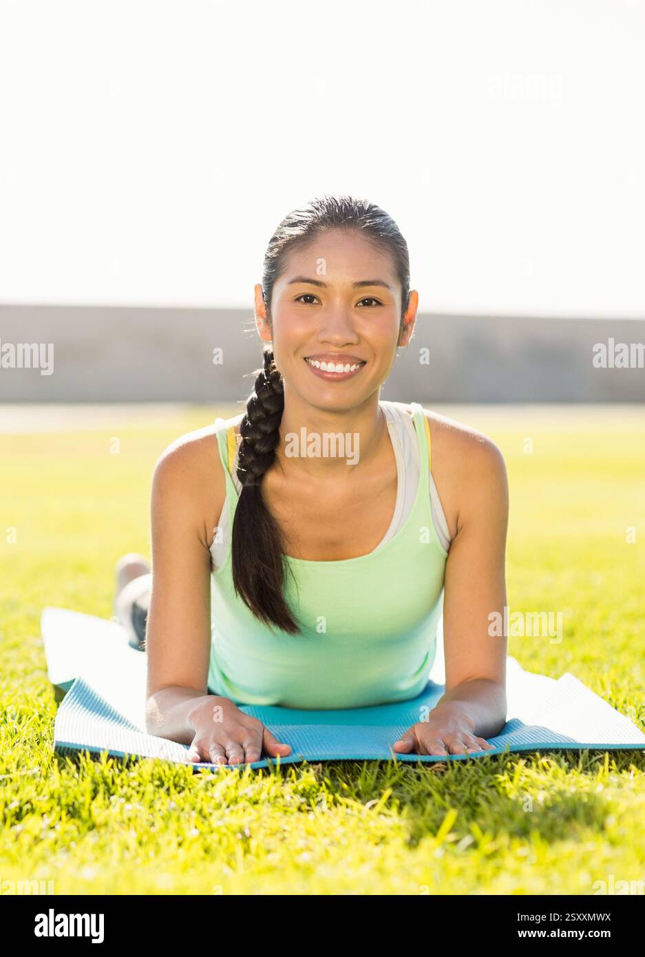 Donna sorridente che pratica yoga sul tappeto all'aperto nel parco soleggiato Foto Stock