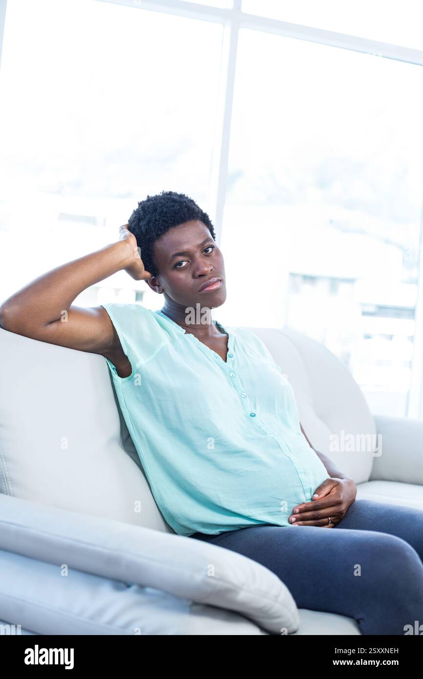 Donna incinta che si rilassa sul divano a casa, che riposa la mano sulla pancia Foto Stock