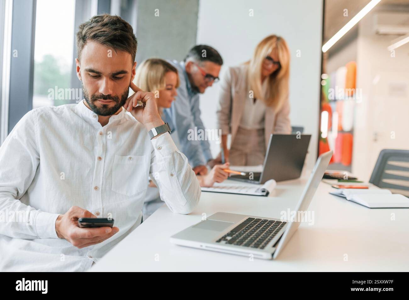 Un giovane uomo alla moda sta lavorando. Un gruppo di professionisti è in ufficio. Foto Stock