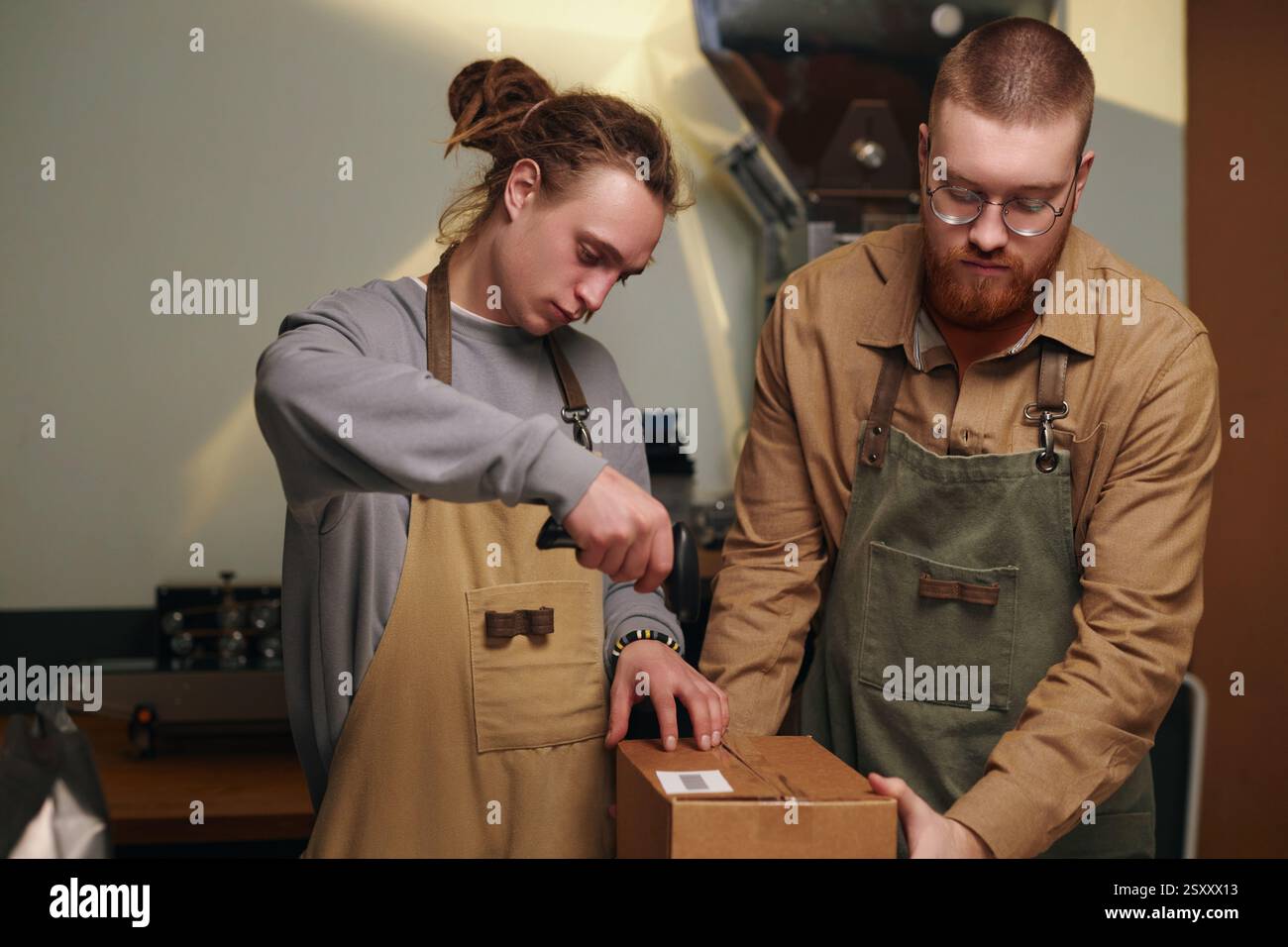 Primo piano medio di un giovane adulto che tiene in mano una scatola di cartone mentre un uomo con dreadlock scansiona il codice a barre Foto Stock