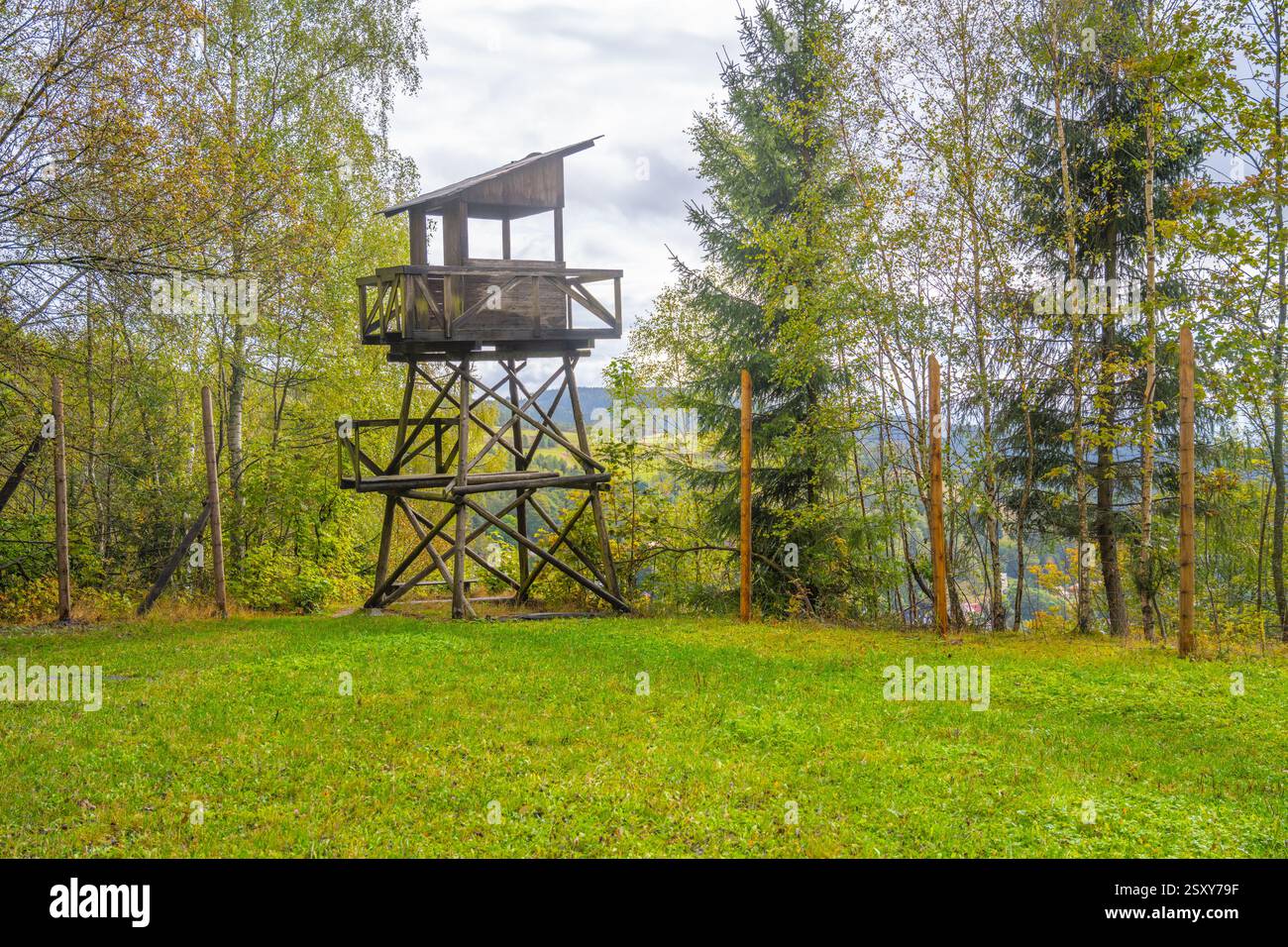 La torre di guardia si erge in modo prominente all'interno del paesaggio del campo di lavoro Svornost a Jachymov, in Cechia, circondato da alberi e aree erbose sotto un cielo nuvoloso. Foto Stock