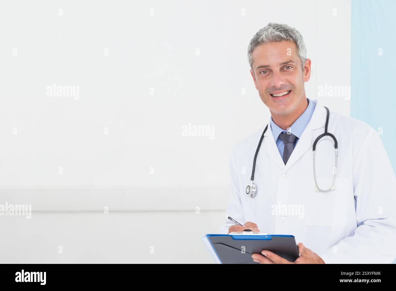 Medico sorridente con gli appunti in ufficio, con stetoscopio e cappotto bianco, spazio copia Foto Stock