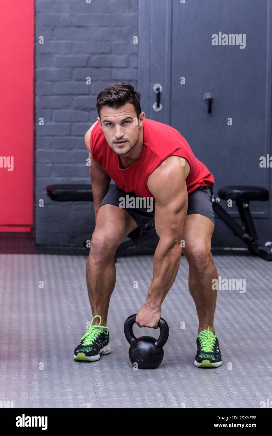 Uomo che solleva kettlebell in palestra, focalizzato sull'allenamento di forza Foto Stock
