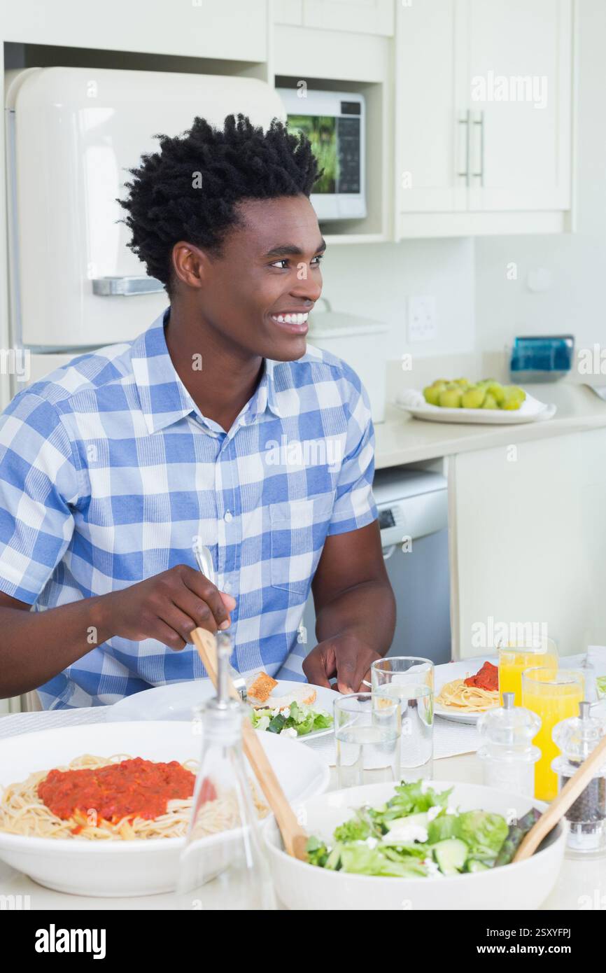 Uomo sorridente che gusta la pasta in una cucina luminosa, sentendosi felice e rilassato Foto Stock