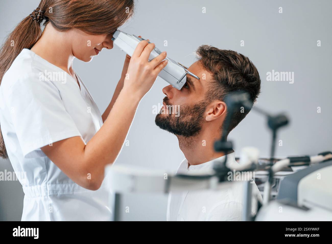 Vista laterale. Visione dell'uomo controllata dal medico in clinica utilizzando uno speciale dispositivo optometrico. Foto Stock