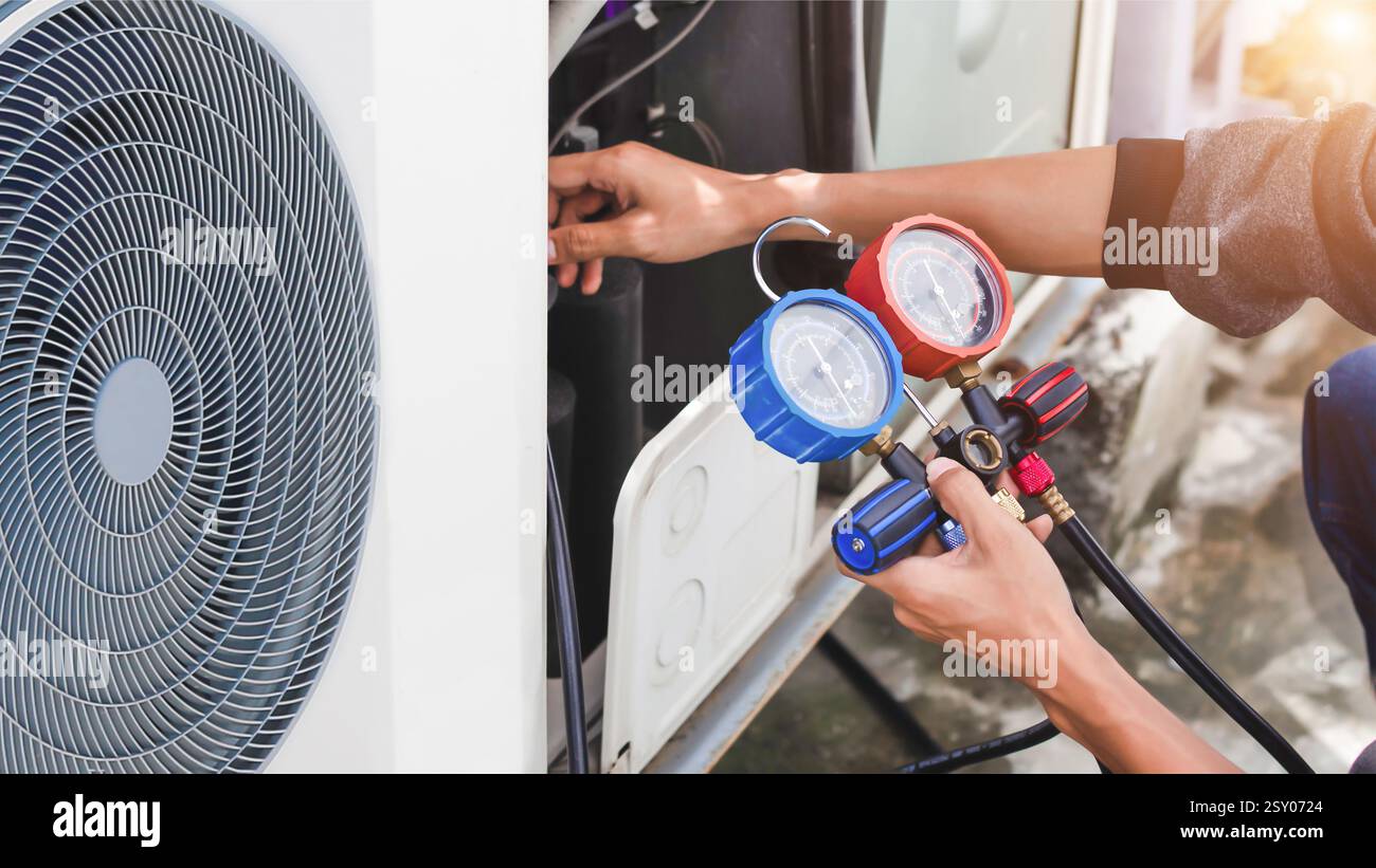 Meccanico addetto alla riparazione dell'aria che utilizza apparecchiature di misurazione per il riempimento dei condizionatori d'aria per impianti industriali e il controllo dell'unità compressore d'aria esterna per la manutenzione. Foto Stock