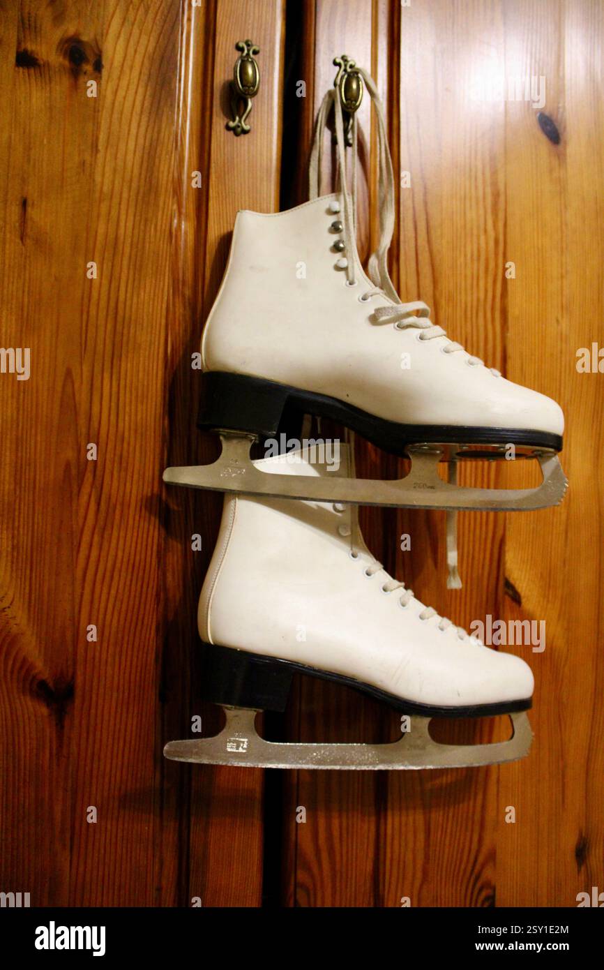 Un paio di pattini di ghiaccio in pelle bianca appesi al gancio dell'armadio in legno della camera da letto, per prepararsi agli sport invernali, scarpe sportive da donna, femminili Foto Stock