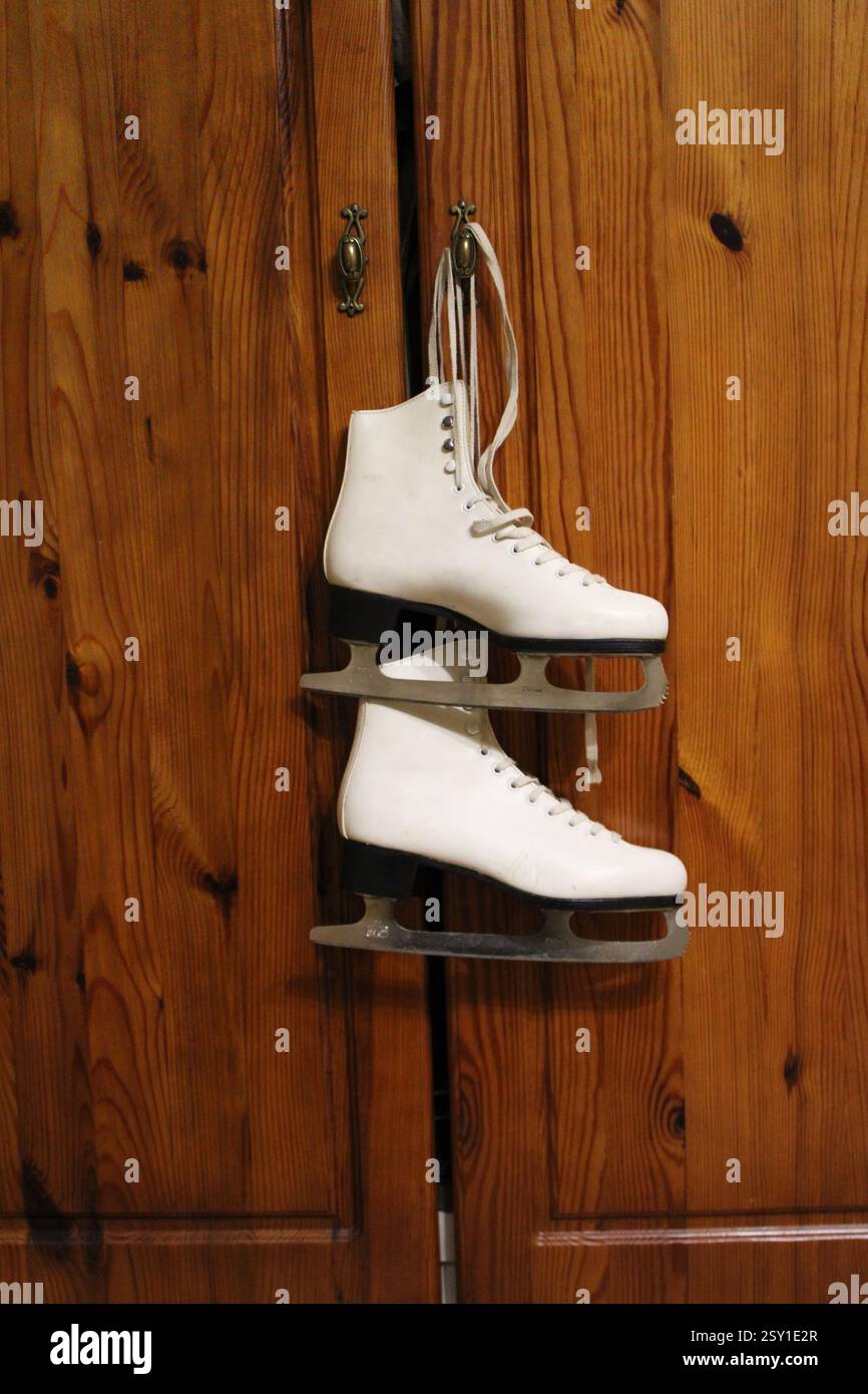 Un paio di pattini di ghiaccio in pelle bianca appesi al gancio dell'armadio in legno della camera da letto, per prepararsi agli sport invernali, scarpe sportive da donna, femminili Foto Stock