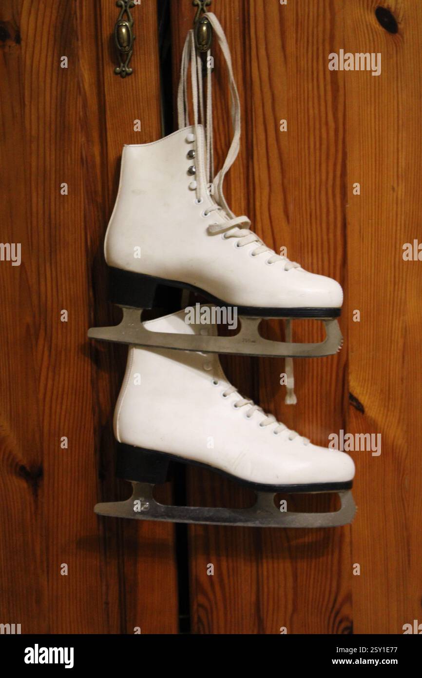 Un paio di pattini di ghiaccio in pelle bianca appesi al gancio dell'armadio in legno della camera da letto, per prepararsi agli sport invernali, scarpe sportive da donna, femminili Foto Stock
