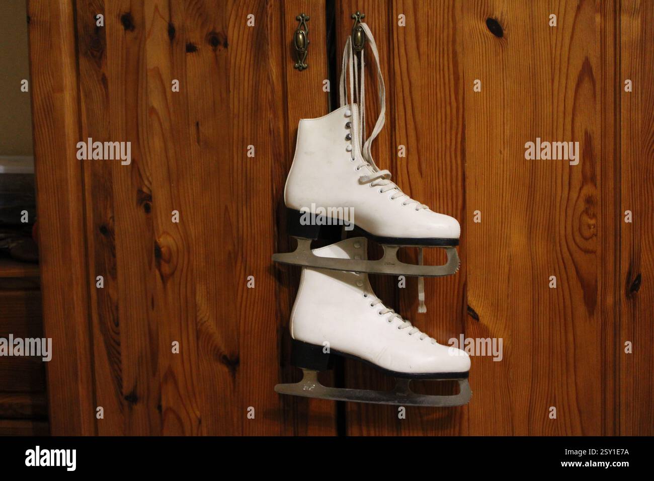 Un paio di pattini di ghiaccio in pelle bianca appesi al gancio dell'armadio in legno della camera da letto, per prepararsi agli sport invernali, scarpe sportive da donna, femminili Foto Stock