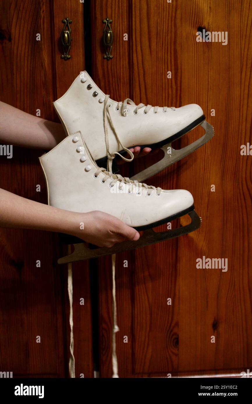 Giovane donna che tiene un paio di pattini di pelle bianca, si prepara per gli sport invernali, scarpe sportive da donna, femminile, attrezzatura, stile di vita attivo felice. Foto Stock