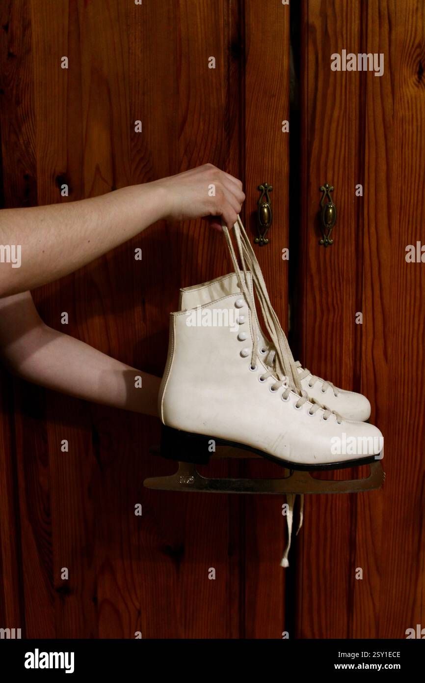 Giovane donna che tiene un paio di pattini di pelle bianca, si prepara per gli sport invernali, scarpe sportive da donna, femminile, attrezzatura, stile di vita attivo felice. Foto Stock